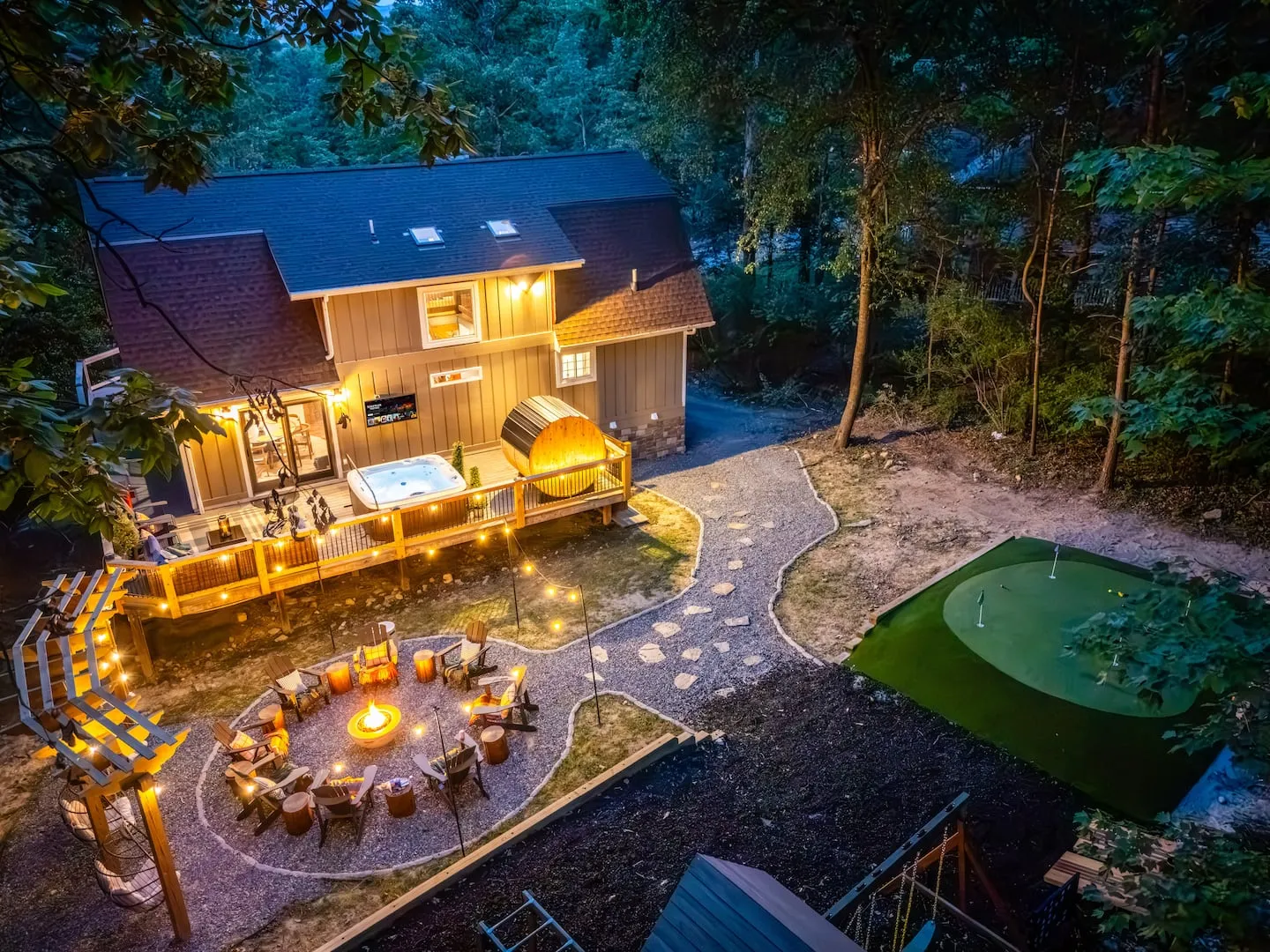 Honey Hollow: aerial view at dusk of the home, lit deck, fire pit garden and putting green